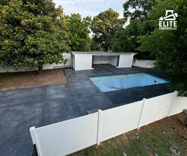 An overhead view of a backyard featuring a newly installed dark gray stamped concrete pool deck and large patio