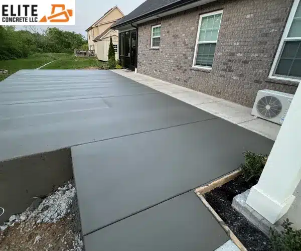 A freshly poured and smoothed concrete patio with clean control joints extension along the side of a brick residential home
