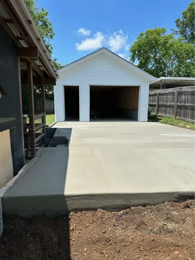 Newly constructed white garage with open doors and a fresh concrete pad by a garage builder.